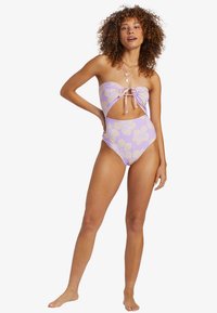 Bikini une pièce imprimé floral violet avec un haut bandeau, des découpes et un devant à nouer. Les bas taille haute rehaussent le design.