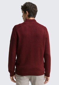 Bordeauxroter Strickpullover mit hohem Kragen, geripptem Saum und Bündchen, mit strukturierter Oberfläche und Raglanärmeln.
