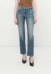 Jean droit bleu clair en denim, doté d'une taille mi-haute, d'un léger délavage et d'un design classique à cinq poches. Assorti à des escarpins noirs.