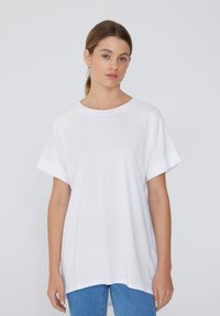 Biała, oversize t-shirt z krótkim rękawem, okrągłym dekoltem i luźnym krojem, wykonana z miękkiego materiału bawełnianego. W połączeniu z niebieskimi dżinsami.
