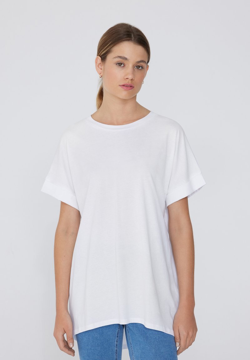 Biała, oversize t-shirt z krótkim rękawem, okrągłym dekoltem i luźnym krojem, wykonana z miękkiego materiału bawełnianego. W połączeniu z niebieskimi dżinsami.