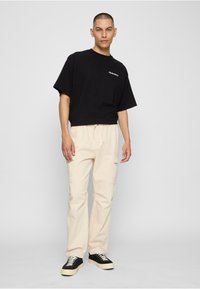 Czarny przycięty t-shirt z białym logo, zestawiony z jasnobeżowymi spodniami cargo z bocznymi kieszeniami. Czarne i kremowe sneakersy. Minimalistyczny design.