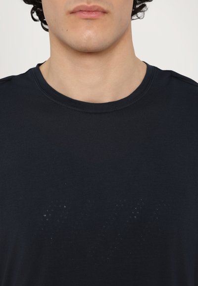 T-shirt bleu marine foncé avec un col rond. Présente un motif subtil dans des teintes plus claires et des détails de couture minimaux sur les épaules.