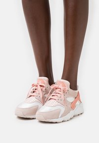 Des baskets en daim rose et maille blanche présentent un col rembourré, des perforations pour une meilleure respirabilité et des semelles en caoutchouc texturé. Lacets dans un rose assorti.