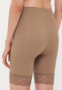 Beige shaper shorts van gladde stof, met een delicate kantafwerking aan de onderkant, die een naadloos ontwerp en een lengte tot halverwege de dij benadrukt.