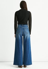 High-waisted, wide-leg blue denim jeans with a faded finish. Pairing with a black textured long-sleeve top and patterned footwear.