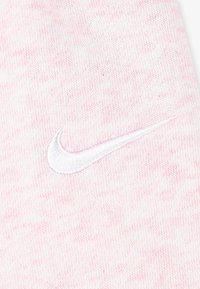 Svetloružová pletenina má bielou vyšívanou Nike swoosh logo, pričom predvádza jemnú textúru a subtilný melírovaný vzor.