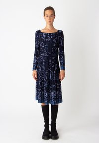Robe à manches longues bleu marine foncé avec un motif floral, dotée d'un décolleté carré, d'une taille cintrée et d'une jupe évasée. Associée à des bottes noires jusqu'aux genoux.