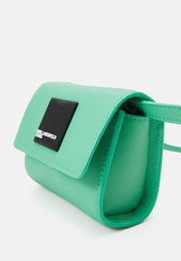 Borsa a tracolla in pelle verde menta con una patch rettangolare nera, chiusura a pattina e una texture liscia.