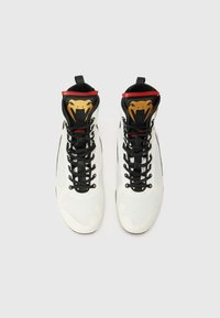 Sneaker alte con una tomaia in rete bianca, lacci neri e colletto nero con un design di serpente dorato e rosso sulla linguetta.