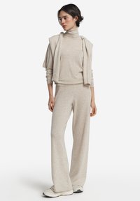 Ljus beige loungewear-set bestående av en polokrage-tröja och vida byxor, tillverkade av mjukt stickad tyg med en avslappnad passform.