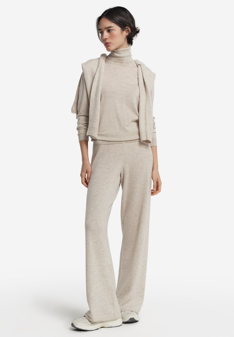 Ljus beige loungewear-set bestående av en polokrage-tröja och vida byxor, tillverkade av mjukt stickad tyg med en avslappnad passform.