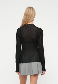Top negru cu mânecă lungă, decorat cu un model transparent și texturat ce prezintă cercuri interconectate. Decolteu rotund cu margini volănaș. Fustă gri plisată.