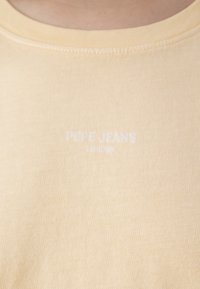 Svetložlté bavlnené tričko s rebrovaným výstrihom. Na prednej strane je potlač s bielym textom "PEPE JEANS LONDON".