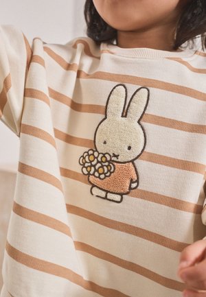 Child wearing a cream and brown striped sweater with an embroidered bunny holding a bouquet of daisies on the front.