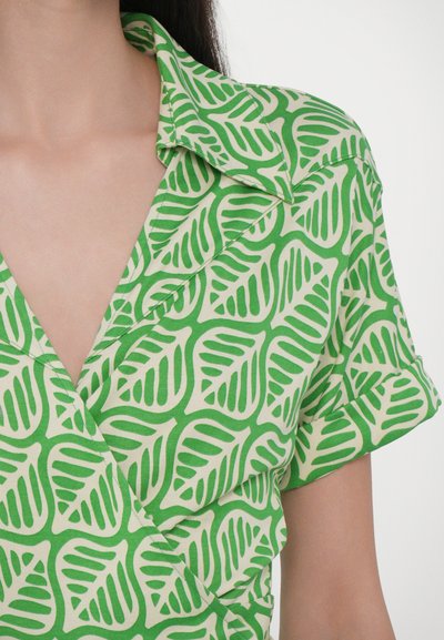 Chemise cache-cœur à manches courtes verte avec un motif de feuilles dans des nuances de vert variées sur fond crème, avec un col classique et une texture lisse.