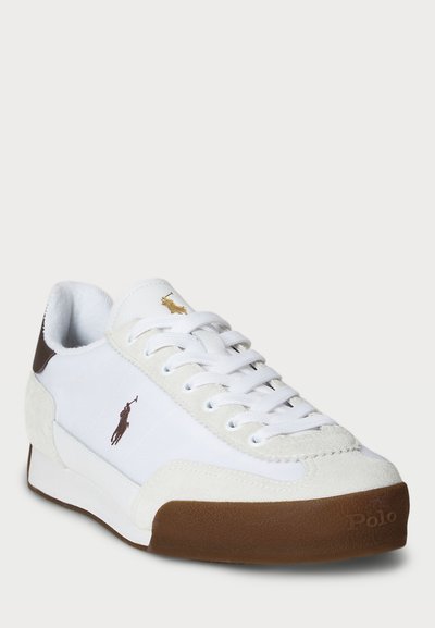 Adidași albi cu accente din suede și talpă din cauciuc maro. Prezintă un design cu șireturi, detalii cu logo aurie și maro pe lateral și o textură netedă.