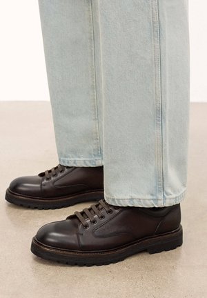 Zapatos de cuero marrón con acentos texturizados, diseño de cordones y suelas de goma negra gruesa, combinados con pantalones de mezclilla azul claro.