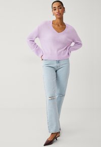 Pull lilas à col en V avec des poignets et un ourlet côtelés, associé à un jean droit déchiré bleu clair et des chaussures à bout pointu bordeau.