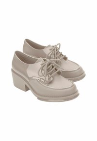 Scarpe in vernice beige con punte arrotondate, lacci piatti e tacchi a blocco. Presentano cuciture a contrasto e una finitura liscia e lucida.