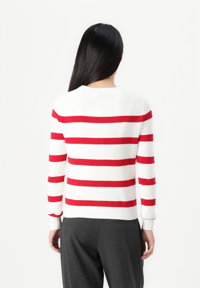 Rot-weißer gestreifter Strickpullover mit rundem Ausschnitt, gerippter Textur und langen Ärmeln; kombiniert mit grauen Hosen.