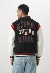 Melnbalta universitātes jakas ar sarkaniem akcentiem, ar uzrakstu "CHICAGO BULLS 1966" un ziedu izšuvumiem uz muguras. Riboti piedurkņu gali un apkakle.