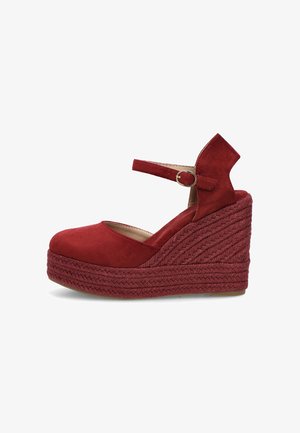 Zapato de tacón cuña de ante rojo con suela plataforma trenzada y correa ajustable en el tobillo con una hebilla redonda de metal.