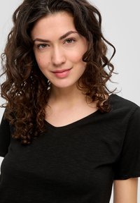Zwarte korte mouwen V-hals t-shirt gemaakt van zachte stof, met een subtiele textuur. Het ontwerp is eenvoudig zonder opvallende patronen of versieringen.