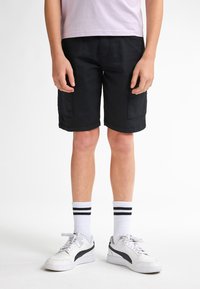 Sorte cargo shorts med sidelommer, glat bomuldsstof og en skræddersyet pasform. Parret med hvide sneakers og stribede ankelstrømper.