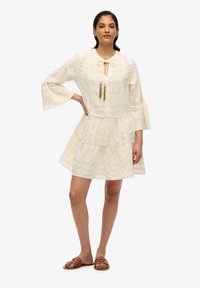 Weißes gemustertes Kleid mit schwingenden Ärmeln, Kragen und Quastenakzenten. Verfügt über ein gestuftes Design und leichtes Material.