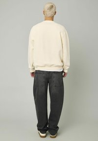 Sweatshirt crème à coupe décontractée, avec des poignets côtelés et un col rond, assorti à un jean en denim gris foncé surdimensionné et des baskets blanches.