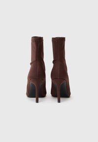 Brune strækstof ankelstøvler med spids tå og høj stiletto-hæl, der har sømløs konstruktion og minimalistisk design.