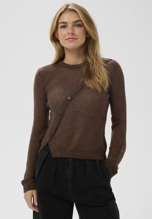 Pulover maro cu mânecă lungă, decolteu rotund și închidere laterală cu nasturi, cu un model texturat tricotat și tiv cu refilet. Asortat cu pantaloni negri.