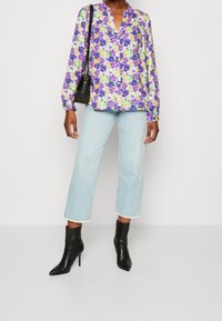 Chemise à manches longues florale avec un motif violet et vert, associée à un jean court bleu clair et des bottines à talons noirs. Sac à main noir.