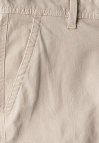 Světle béžová bavlněná tkanina s hladkou texturou, obsahující vertikální šev a pás s prošitým okem.