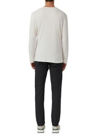 Witte blouse met lange mouwen en een zachte textuur, gecombineerd met donkere grijze broeken. Model draagt witte sneakers met groene accenten.