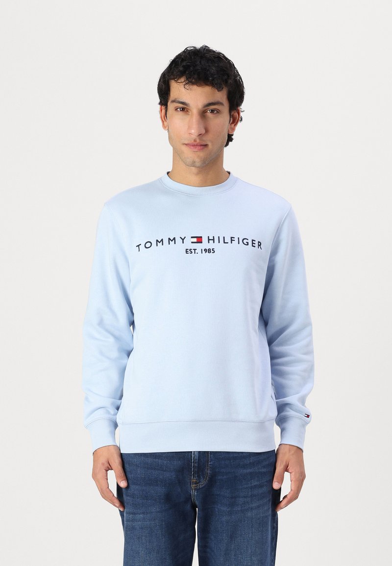 Šviesiai mėlynas apvalus kaklas su ilgomis rankovėmis ir gumuotais rankogaliais. Krūtinėje yra "TOMMY HILFIGER EST. 1985" logotipas.