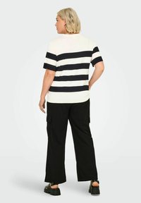 Top a righe a maniche corte, bianco e navy, abbinato a pantaloni neri a gamba larga. Il top ha un collo rotondo e una vestibilità comoda.
