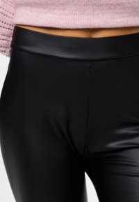 Črne legice iz umetnega usnja z gladkim, sijočim videzom. Imajo širok, raven pas in brezšivno zasnovo.