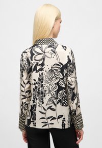 Blusa a maniche lunghe color crema con motivo floreale nero. Presenta un collo alla francese e polsini decorati, realizzata in tessuto liscio.