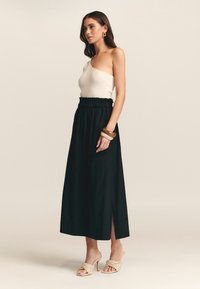 Beige ribbed top yhdistettynä mustaan, nilkkapituiseen hameeseen, jossa on joustava vyötärö ja sivuhalkio. Lisäksi jaloissa on punotut korolliset mokkasiinit.