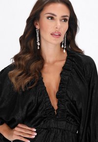 Fekete, fodros blúz mély V-nyakkivágással, texturált anyagból készült, hosszú ujjakkal és elasztikus derékrésszel.