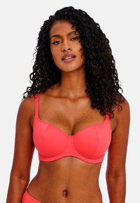 Coral pink bra with underwire, thin adjustable straps, and smooth fabric. Cups feature vertical seams for support. Simple, sleek design.