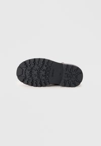 Semelle de chaussure en caoutchouc noir avec un motif de semelle texturé, présentant des rainures et des accents circulaires pour une meilleure adhérence et traction.