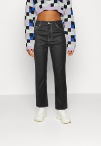 Jeans pretos de cintura alta com corte reto, apresentando costuras brancas em contraste e bolsos frontais, combinados com uma blusa crop de padrão quadriculado multicolorido.