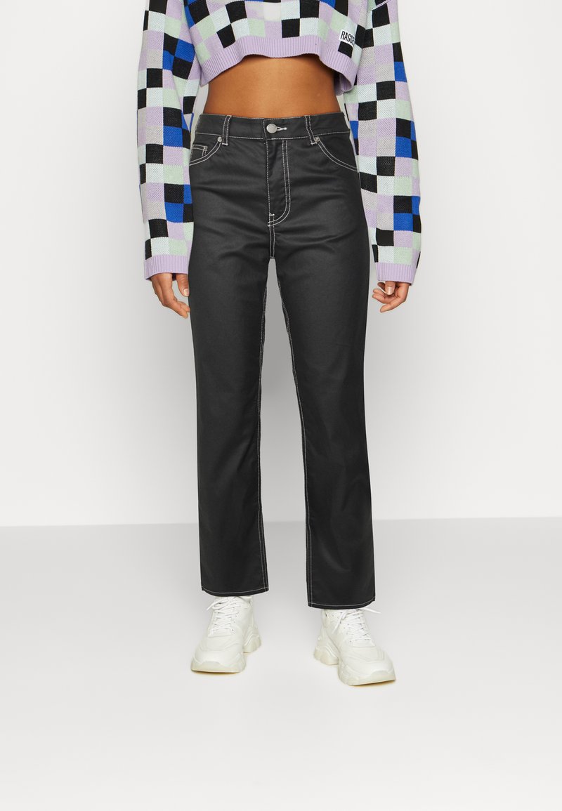Jeans pretos de cintura alta com corte reto, apresentando costuras brancas em contraste e bolsos frontais, combinados com uma blusa crop de padrão quadriculado multicolorido.