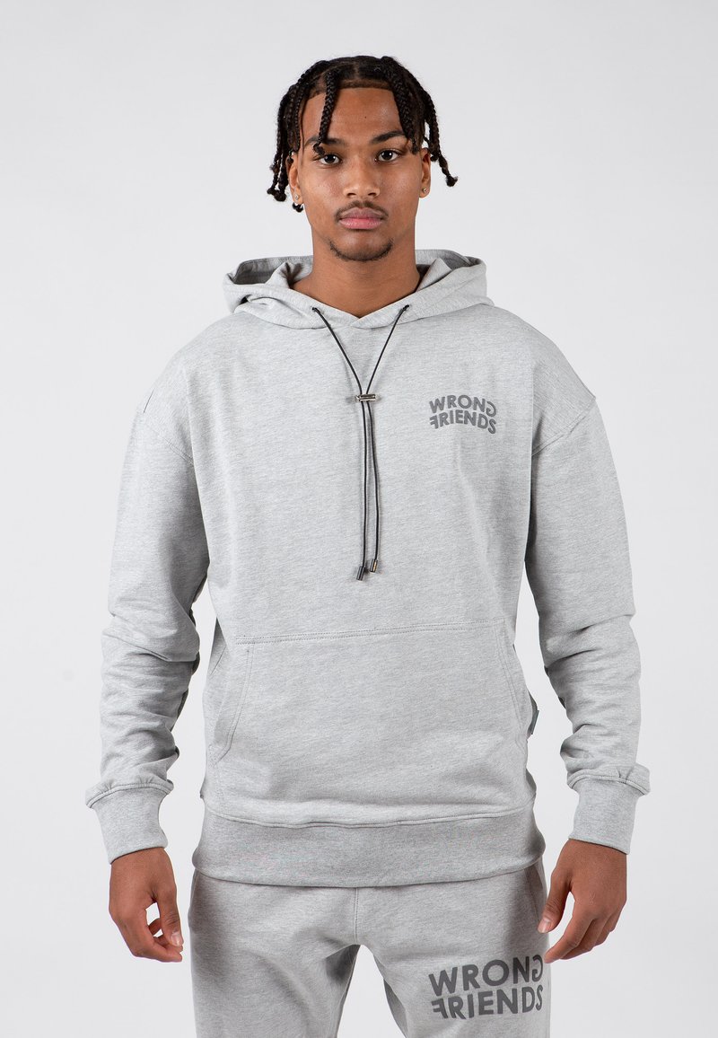 Szary hoodie z sznurkiem, w luźnym kroju, z kieszenią z przodu i napisem "WRONG FRIENDS" na klatce piersiowej. Materiał wydaje się miękki i gładki.