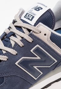 Marinblå New Balance 574 sneakers med övre i mesh och mocka, krämfärgade snören, stort vitt 'N'-logotyp och texturerad detalj på tungan.