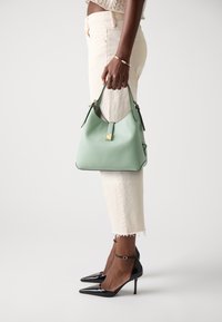 Mint green leather hobo bag with a textured finish, featuring a gold hardware accent. Worn with cream jeans and black patent stilettos.