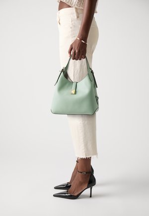 Sac hobo en cuir vert menthe avec une finition texturée, doté d'une quincaillerie dorée. Porté avec un jean crème et des escarpins noirs en vernis.